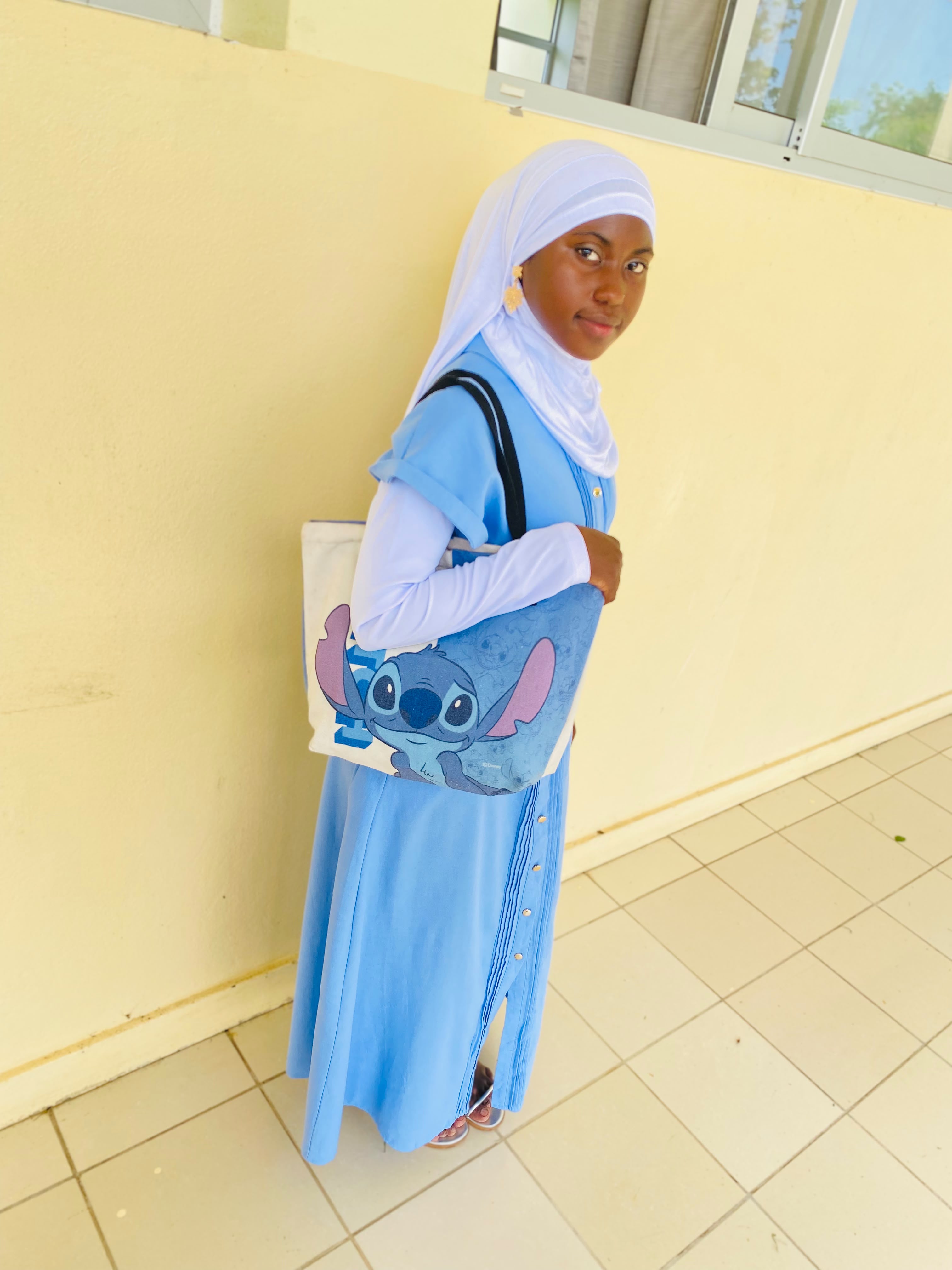Tuayibah, sorridente, com hijab azul e um peluche de Stitch nos braços.